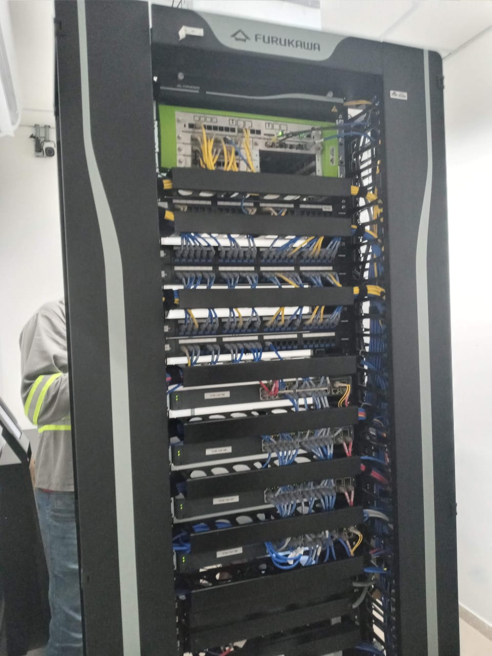 Técnico ao lado de rack Furukawa com cabeamento estruturado CAT6